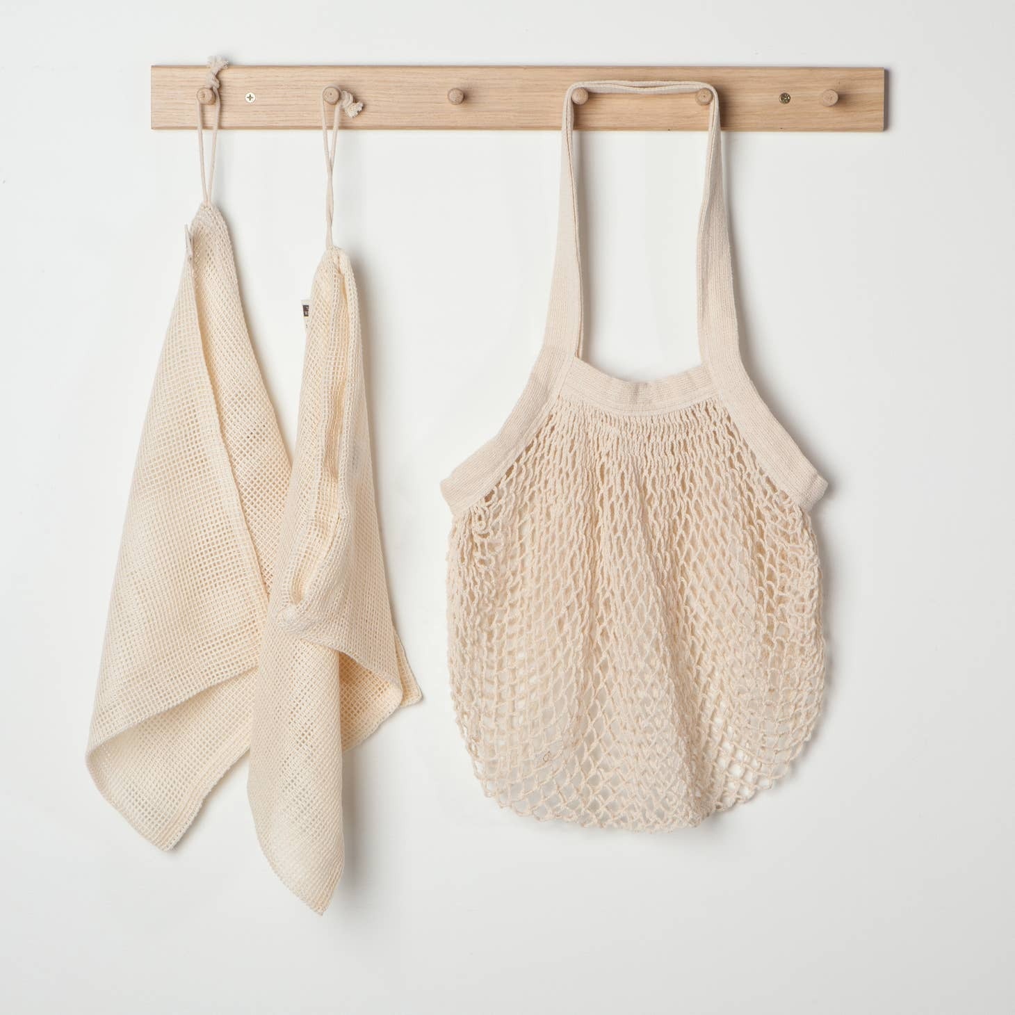 Natural cotton tote bag hangs on wooden hooks with mesh bulk bags on a white background