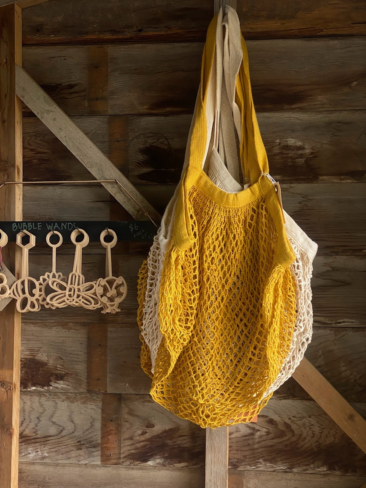 Yellow mesh market tote hangs on a hook with a rustic wooden background.