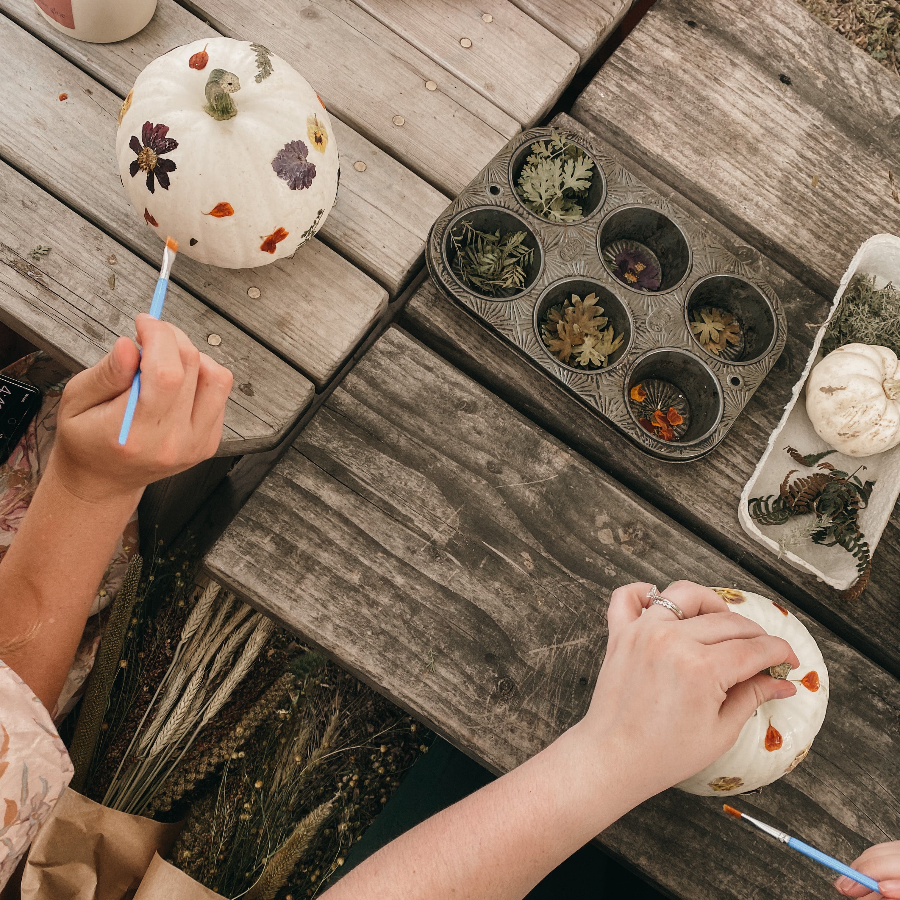 Two people painting small pumpkins on a wooden table.