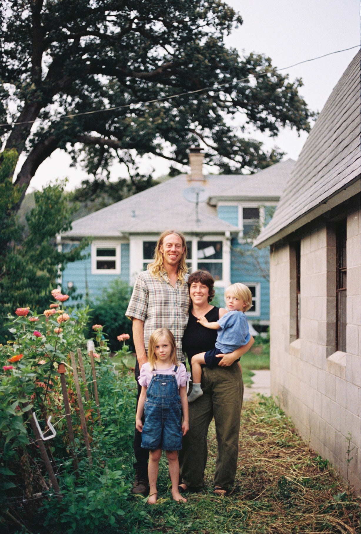 Family of four standing in a garden with a house in the background